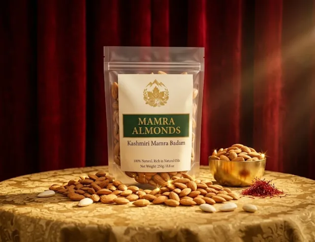 Valley Origin Kashmiri Mamra Badam 250 g pouch on a gold cloth beside a brass bowl of almonds, with red velvet curtains behind